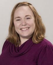 Dr. April Megginson smiling with medium length red hair and wearing a cowl neck raspberry colored sweater