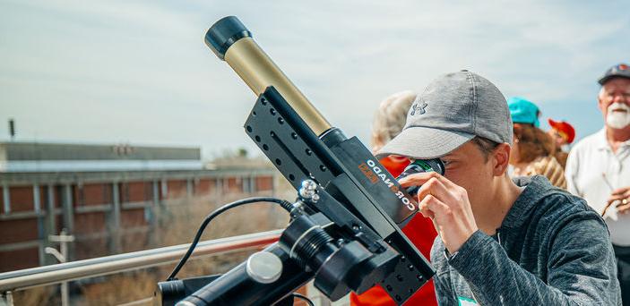 A student gazes in a telescope at the eclipse.